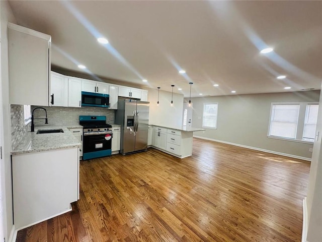 kitchen with decorative backsplash, appliances with stainless steel finishes, wood finished floors, a peninsula, and a sink