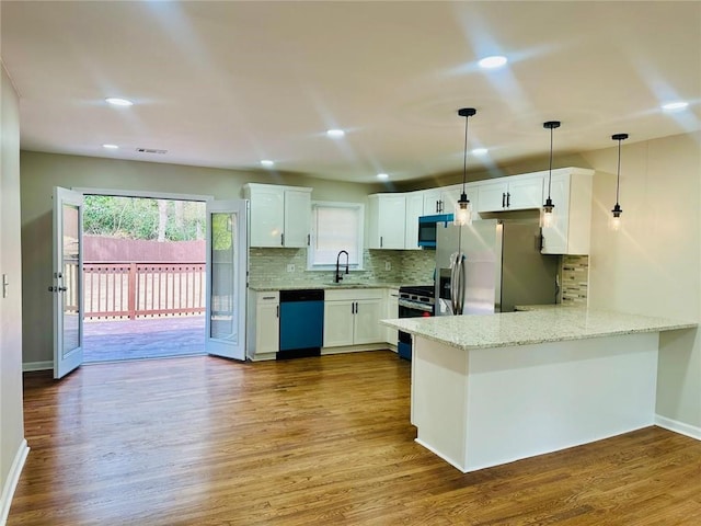 kitchen featuring stainless steel appliances, a peninsula, wood finished floors, a sink, and tasteful backsplash