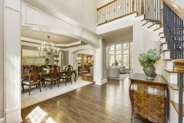 interior space with arched walkways, wood finished floors, a high ceiling, and an inviting chandelier
