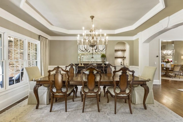 dining area with a tray ceiling, wood finished floors, ornamental molding, arched walkways, and a chandelier