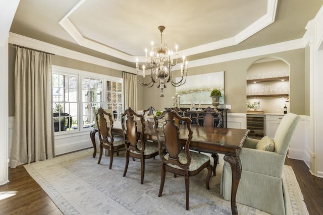 dining room featuring crown molding, a chandelier, a raised ceiling, dark wood-type flooring, and wine cooler