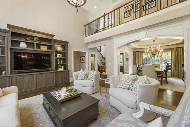 living area with arched walkways, a towering ceiling, wood finished floors, and a chandelier