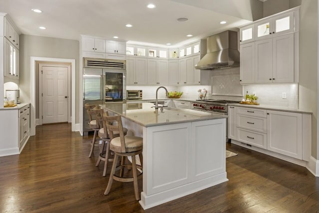 kitchen featuring high end appliances, wall chimney range hood, white cabinetry, and dark wood-style flooring