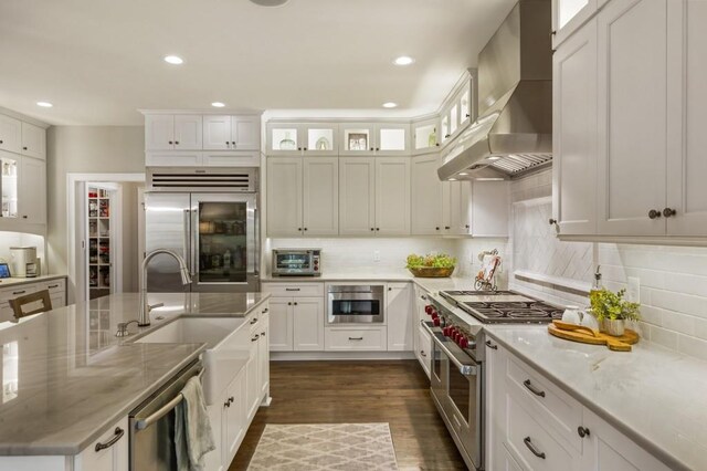 kitchen featuring high end appliances, white cabinets, light stone counters, and wall chimney range hood