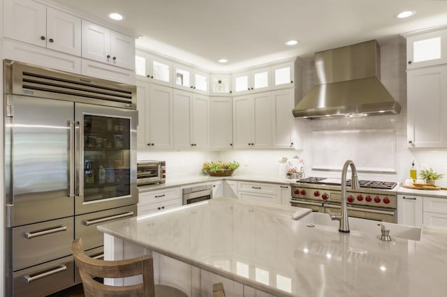 kitchen with white cabinets, wall chimney exhaust hood, light stone counters, and premium appliances