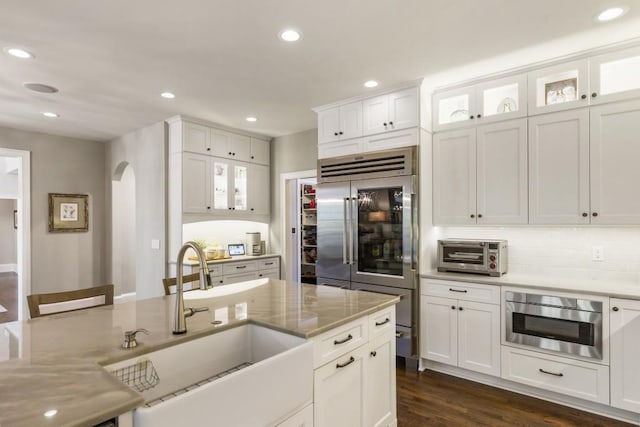 kitchen featuring built in refrigerator, tasteful backsplash, a sink, white cabinets, and dark wood-type flooring