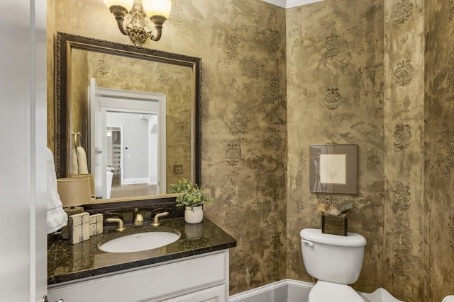 bathroom with toilet, vanity, wallpapered walls, and baseboards