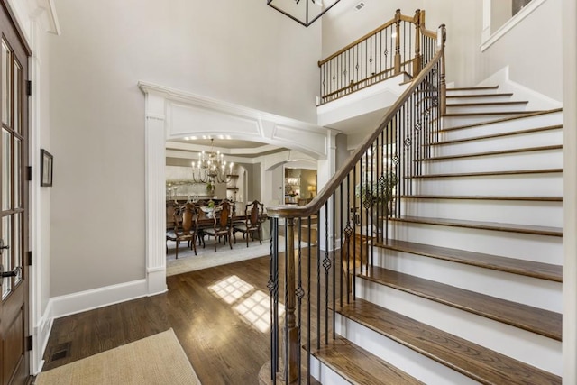 entrance foyer featuring arched walkways, a towering ceiling, a chandelier, wood finished floors, and stairway