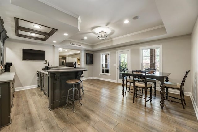 kitchen featuring baseboards, dark cabinetry, wood finished floors, ornamental molding, and a raised ceiling