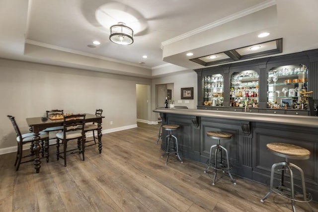 bar featuring bar area, baseboards, crown molding, and dark wood-type flooring