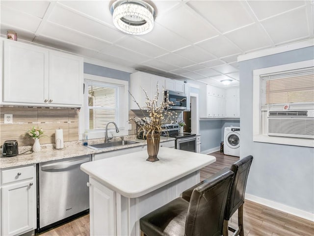 kitchen featuring appliances with stainless steel finishes, white cabinetry, a sink, washer / dryer, and light wood-type flooring