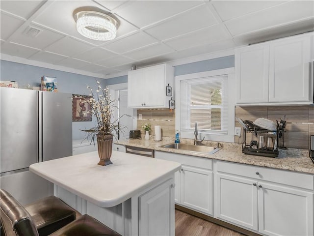 kitchen featuring tasteful backsplash, appliances with stainless steel finishes, white cabinets, a sink, and a kitchen bar