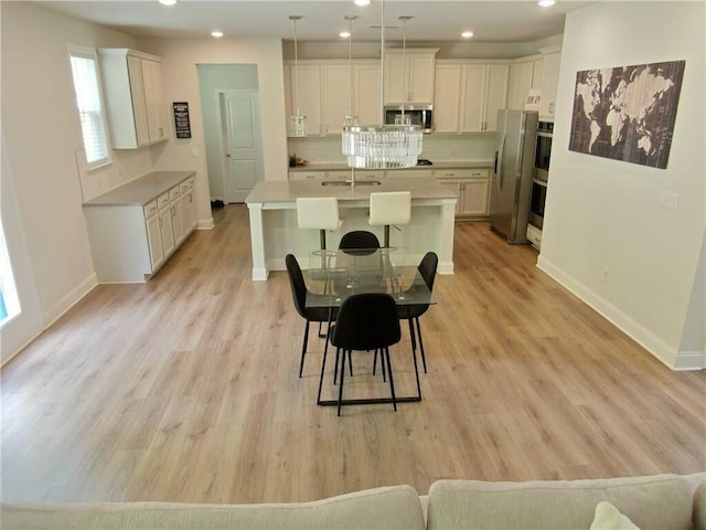 kitchen featuring stainless steel appliances, tasteful backsplash, pendant lighting, a center island with sink, and white cabinets