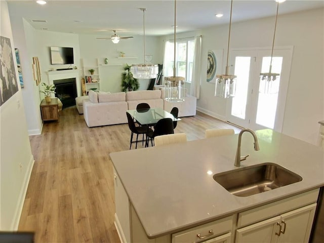 kitchen featuring a kitchen island with sink, sink, ceiling fan, light wood-type flooring, and decorative light fixtures