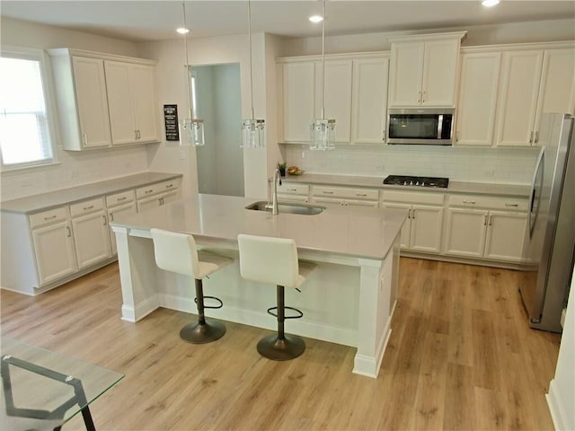 kitchen with pendant lighting, white cabinets, sink, an island with sink, and appliances with stainless steel finishes