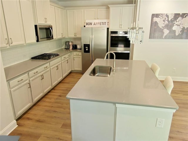 kitchen featuring backsplash, a center island with sink, sink, appliances with stainless steel finishes, and white cabinetry