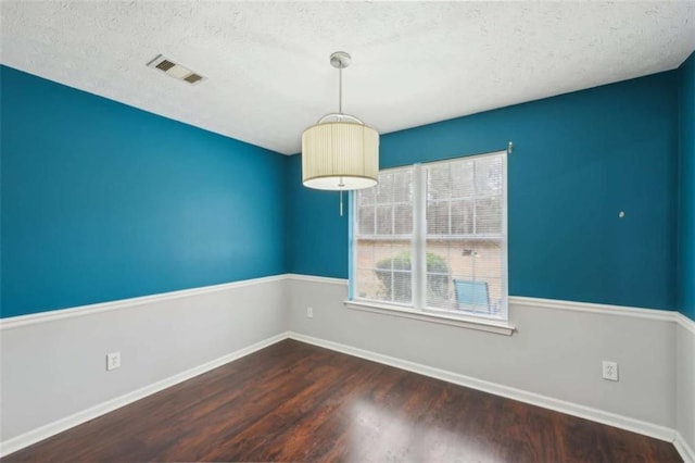 unfurnished dining area featuring visible vents, a textured ceiling, baseboards, and wood finished floors