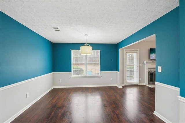 spare room with visible vents, a fireplace with flush hearth, a textured ceiling, and wood finished floors