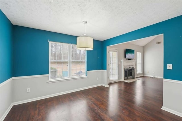 unfurnished living room featuring a fireplace, wood finished floors, visible vents, and a textured ceiling