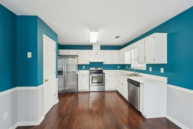 kitchen with dark wood-style flooring, a sink, stainless steel appliances, light countertops, and white cabinets