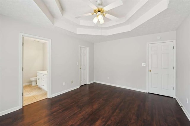 unfurnished bedroom with a raised ceiling, wood finished floors, baseboards, and connected bathroom