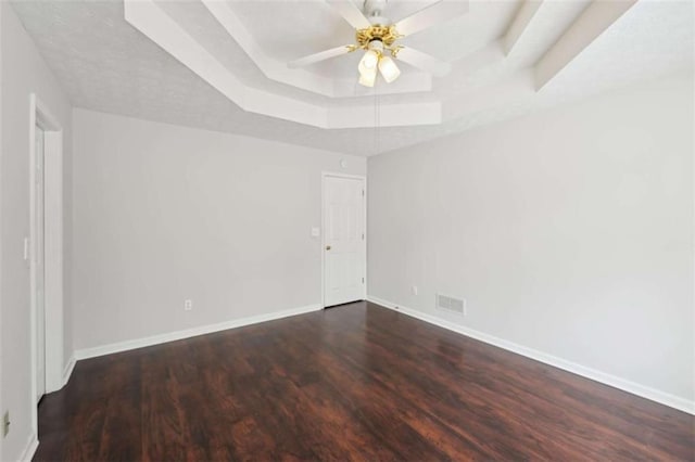 spare room featuring visible vents, baseboards, a tray ceiling, wood finished floors, and a ceiling fan