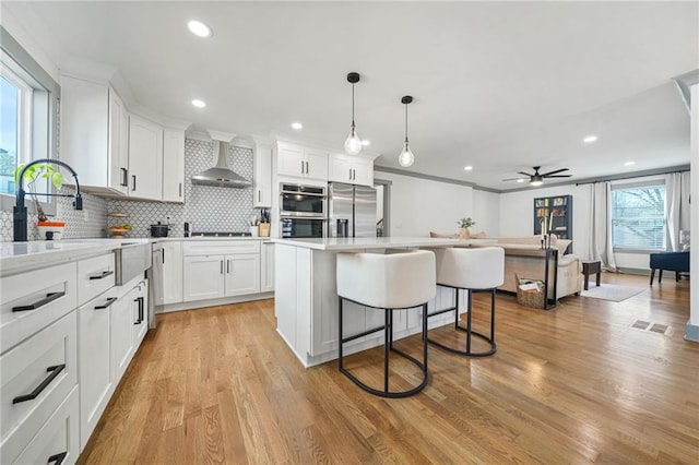 kitchen with white cabinetry, a kitchen island, and wall chimney range hood