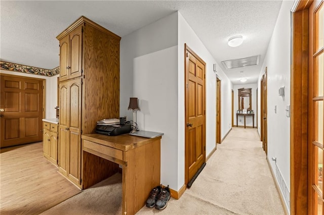 hallway with a textured ceiling and light colored carpet