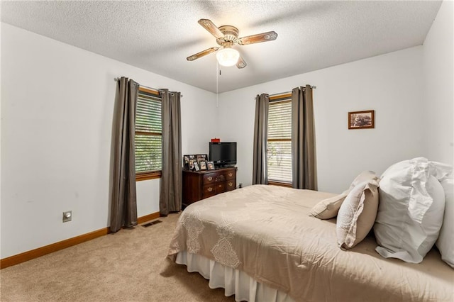 bedroom with light colored carpet, multiple windows, a textured ceiling, and ceiling fan