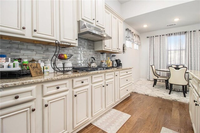 kitchen with decorative backsplash, light stone counters, wood-type flooring, and stainless steel gas cooktop