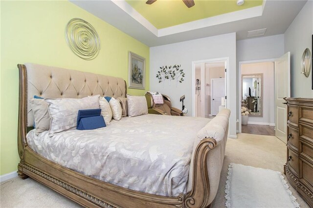 bedroom featuring ensuite bathroom, ceiling fan, light carpet, and a tray ceiling