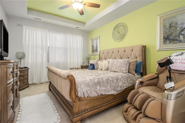 bedroom with light colored carpet, a raised ceiling, and ceiling fan