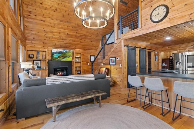 living room with light wood-type flooring, wood walls, a barn door, and a lit fireplace