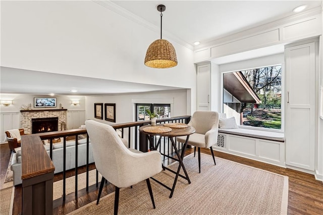 dining space featuring a decorative wall, a towering ceiling, ornamental molding, a brick fireplace, and dark wood-style floors