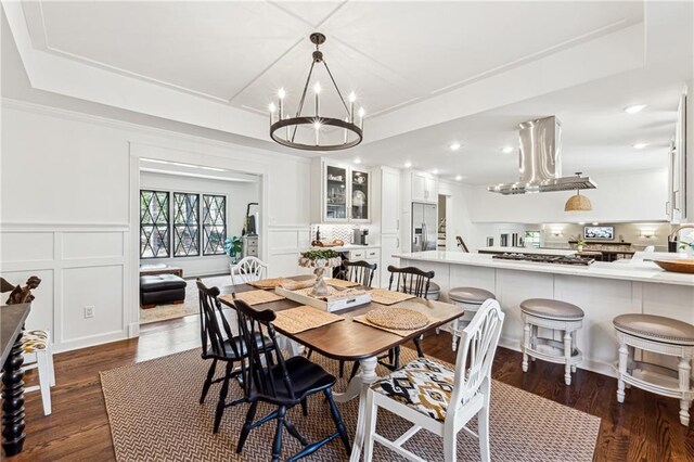 dining space featuring a raised ceiling, a decorative wall, dark wood-type flooring, and wainscoting