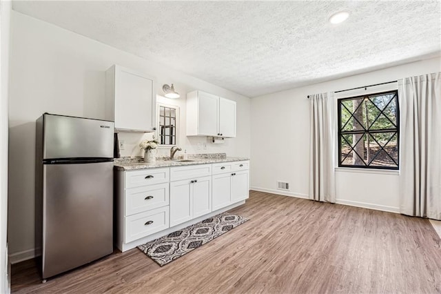 kitchen featuring light wood-type flooring, freestanding refrigerator, white cabinets, and light stone countertops