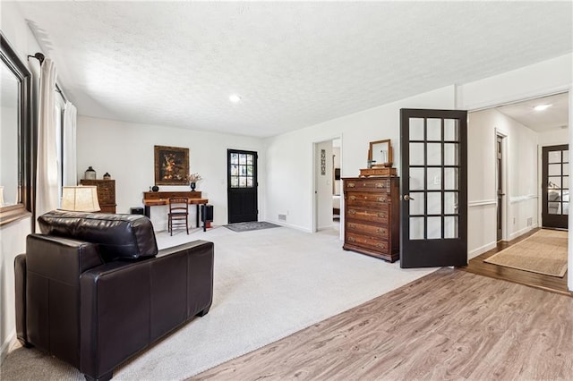 carpeted living area featuring a textured ceiling, wood finished floors, and baseboards