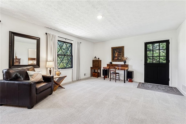 living area with a textured ceiling, plenty of natural light, and light colored carpet