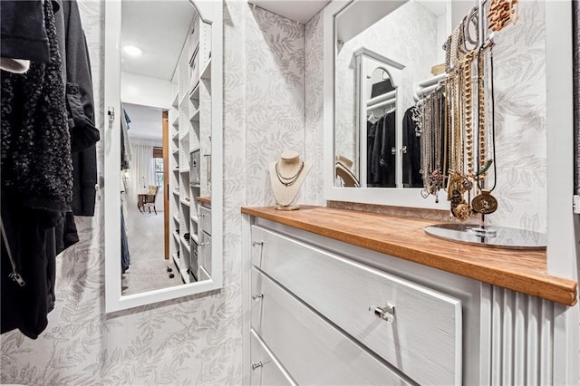 bathroom with a spacious closet, vanity, and wallpapered walls