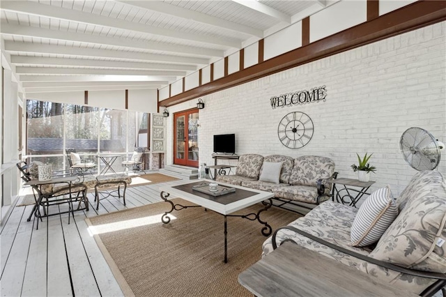 living room with a sunroom, lofted ceiling with beams, brick wall, and wood finished floors