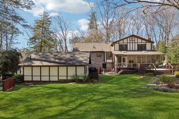 rear view of property featuring a sunroom, a chimney, a deck, and a lawn