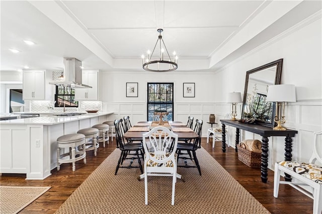 dining room with dark wood-type flooring, a tray ceiling, a notable chandelier, and a decorative wall