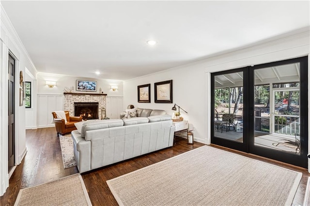 living room featuring french doors, a wainscoted wall, dark wood finished floors, ornamental molding, and a brick fireplace