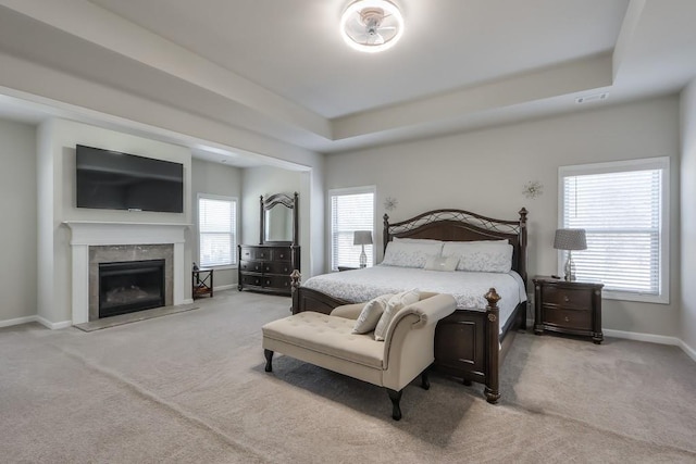 carpeted bedroom with a fireplace and a raised ceiling