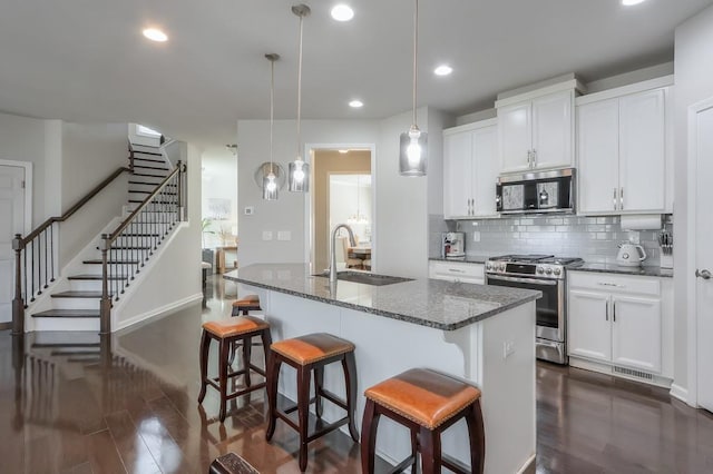 kitchen with pendant lighting, sink, stainless steel appliances, an island with sink, and white cabinets