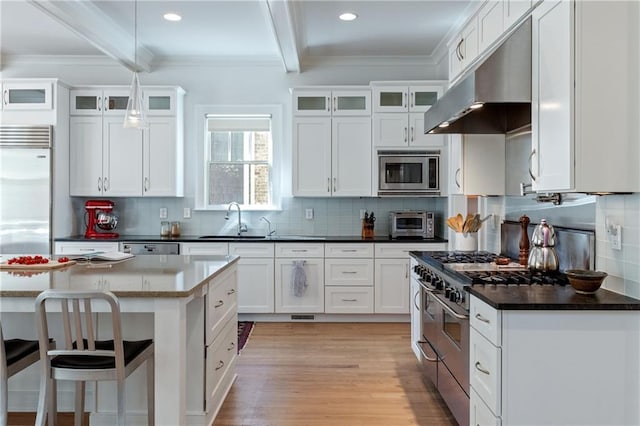 kitchen with light wood finished floors, tasteful backsplash, under cabinet range hood, built in appliances, and beam ceiling