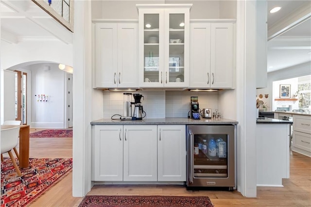 bar with wine cooler, light wood-style flooring, arched walkways, and backsplash