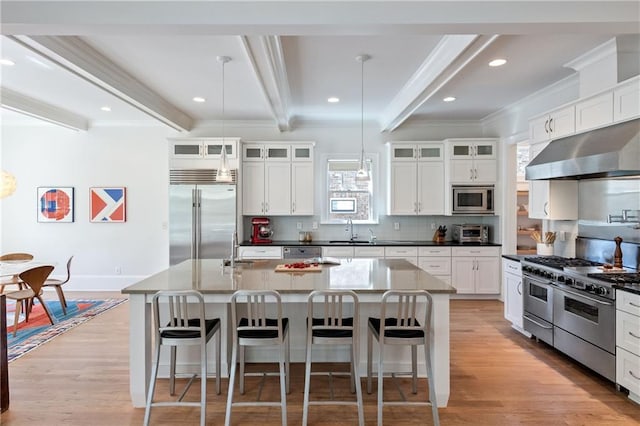 kitchen featuring under cabinet range hood, built in appliances, beamed ceiling, and crown molding