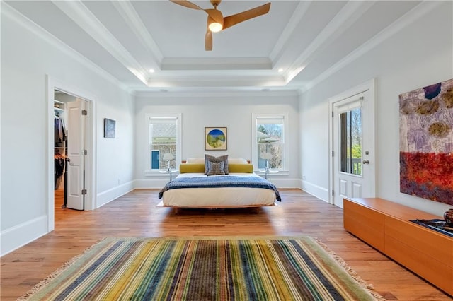 bedroom with a raised ceiling, ornamental molding, light wood-style floors, baseboards, and a spacious closet