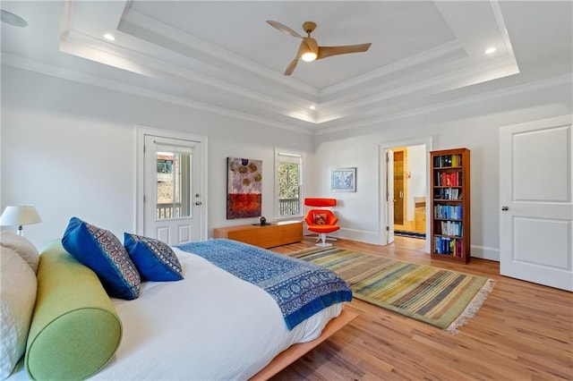 bedroom with a raised ceiling, wood finished floors, baseboards, and ornamental molding